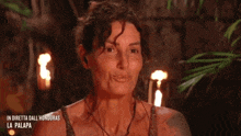 a woman is smiling with her hands folded in front of a fire in a jungle .