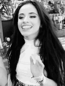 a black and white photo of a woman with long hair smiling and giving the middle finger .