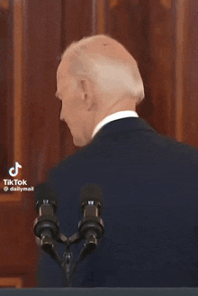a man in a suit and tie is speaking into a microphone and the word joke is on the screen