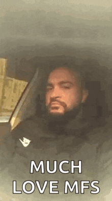a man with a beard is sitting in a car with his eyes closed and the words `` much love mfs '' .