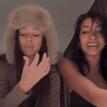 a woman wearing a furry hat stands next to another woman