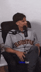 a man in a houston jersey sits in a chair in front of a microphone