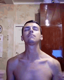 a shirtless man stands in front of a wall with a calendar on it