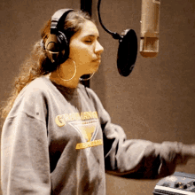 a woman wearing headphones and a gray sweatshirt that says grad king on it