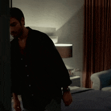 a man in a black shirt sits on a bed in a bedroom
