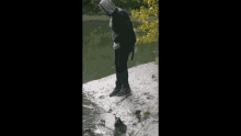 a man in a hoodie is standing on a rock near a lake