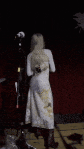 a woman in a white dress stands in front of a microphone