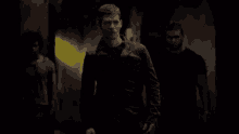 a man in a black jacket is walking in a dark room with two other men .