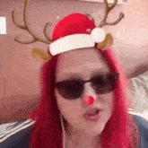 a woman with red hair wearing sunglasses and a santa hat with reindeer antlers .