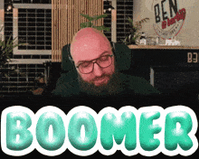 a bald man with glasses and a beard is sitting in front of a screen that says boomer