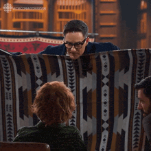 a man and a woman are sitting in front of a blanket that says cbcdragonsden on the bottom