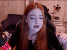 a girl with long red hair is sitting in a chair with her eyes closed .