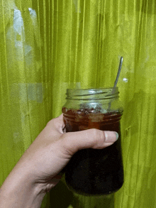 a person is holding a jar with a spoon in it in front of a green curtain
