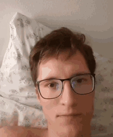 a man wearing glasses is laying on a bed with a pillow behind him
