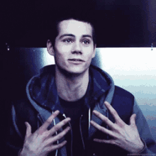 a young man wearing a hoodie and a black shirt is talking with his hands outstretched