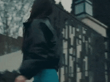 a woman wearing a blue dress and a black jacket is walking down the street .