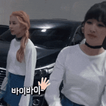 two girls are standing in front of a car and one of them is wearing a white sweater