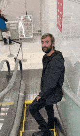 a man with a beard is standing on an escalator in front of a sign that says 1 20