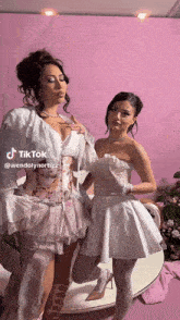 two women are posing for a picture in front of a pink background .