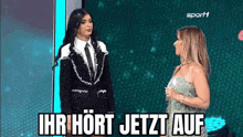 a woman in a suit and tie is standing next to a woman in a green dress on a stage .
