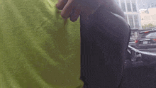 a person in a green shirt is standing next to a black car in a parking lot .