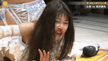 a female wrestler with blood on her face is laying on the ground during a match