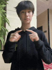 a young man wearing a black hoodie is pointing at his sleeve