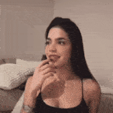 a woman in a black tank top is sitting on a couch with her hand to her mouth .