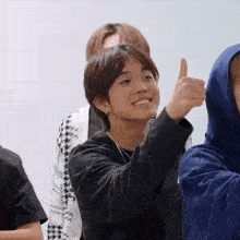 a young boy is giving a thumbs up sign while sitting in a room with other people .