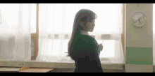 a girl in a green sweater is standing in front of a window holding a pencil .