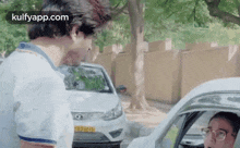 a man is standing next to a car talking to another man .
