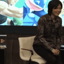 a man sits in a chair in front of a screen with a frog on it