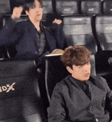 a man in a suit sits next to another man in a theater seat that says 3dx on it