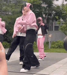 a group of people in pink clothes are dancing on the sidewalk .
