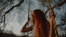 a woman with long red hair is swinging on a rope swing