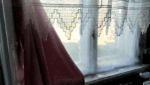 a window with a white lace curtain and a pink curtain