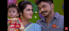 a man and a woman are holding a baby in front of a sun tv logo