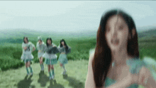 a group of girls are dancing in a field with a woman standing in the foreground .