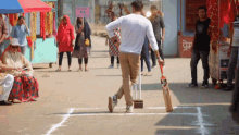 a man is holding a ss cricket bat in front of a sign that says ' no entry vs '
