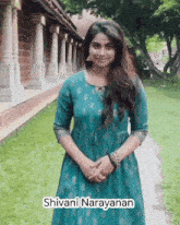 a woman in a blue dress is standing in front of a building with the name shivani narayanan on it