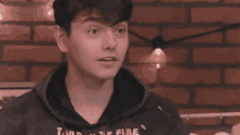 a young man in a black hoodie is standing in front of a brick wall and looking at the camera .