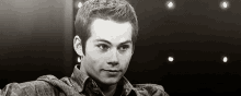 a black and white photo of a young man wearing a plaid shirt and looking at the camera .