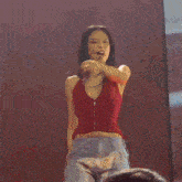 a woman in a red top is dancing in front of a pink wall