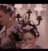 a woman with a flower crown on her head is smoking a cigarette while another woman looks on .