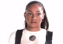 a young woman wearing a necklace and earrings is looking at the camera .