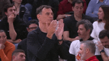 a man applauds while sitting in the stands of a basketball game