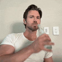 a man in a white shirt is drinking water from a glass