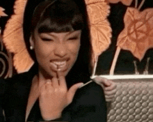 a woman in a black dress is smiling and holding her finger to her mouth