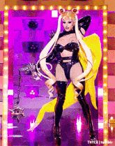 a drag queen is wearing a sailor moon costume and holding a yellow cape while standing on a stage .