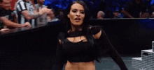 a woman in a black crop top is standing in front of a crowd in a wrestling ring .